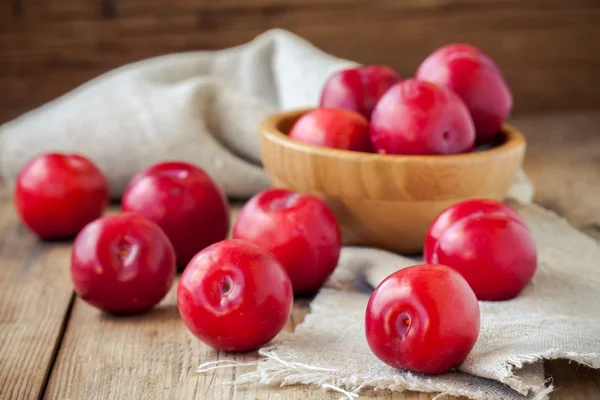 Red plums in a bowl on an old rustic background — Stock Photo, Image