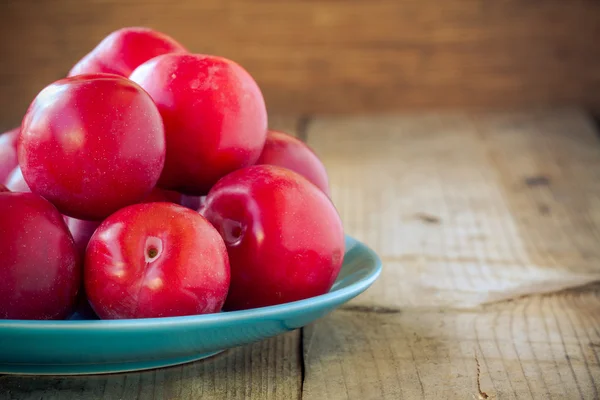 Red plums in a blue plate on a rustic wooden background — Stock Photo, Image