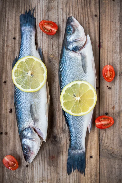 Two raw seabass fish with lemon and cherry tomatoes on wooden ba — Stock Photo, Image