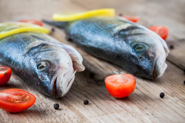Two raw seabass fish with cherry tomatoes on a rustic wooden bac — Stock Photo, Image