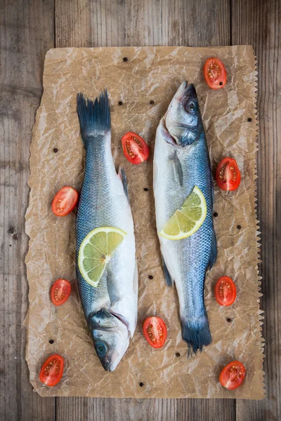 Zwei rohe Seebarschfische mit einer Zitronenscheibe und Kirschtomaten auf — Stockfoto