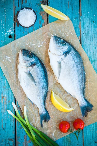 Two raw dorada fishes with lemon, green onions and cherry tomatoes — Stock Photo, Image
