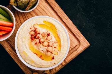Zeytinyağlı humus ve sebze çubuklu nohut ve koyu taşlı arka planda çıtır ekmek. Üst görünüm, kopyalama alanı ile.