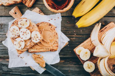 Ahşap zemin üzerinde muz dilimleri olan fıstık ezmeli tost. Kahvaltı tostları..