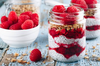 Chia Pudingi. Sağlıklı vanilyalı ahududu pudingi cam kavanozda taze böğürtlen ve ahşap arka planda granola yulaflı.