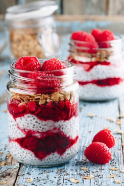 Chia Pudingi. Sağlıklı vanilyalı ahududu pudingi cam kavanozda taze böğürtlen ve ahşap arka planda granola yulaflı.