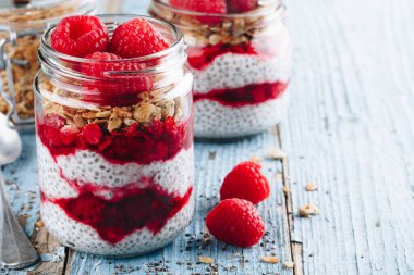 Chia Pudingi. Sağlıklı vanilyalı ahududu pudingi cam kavanozda taze böğürtlen ve ahşap arka planda granola yulaflı.