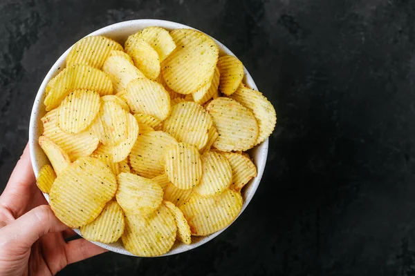Patates cipsi. Elinde patates cipsi kasesi olan kadın elleri koyu taştan bir arka planda, üst manzarada fotokopi alanı var..