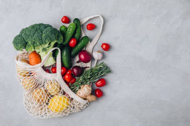 Sebzeli ağ torbası. Organik brokoli, domates, salatalık, havuç, soğan, limon, sarımsak, zencefil, biberiye ve patates. Sıfır atık, plastiksiz konsept. Sağlıklı beslenme ve detoks. Üst görünüm