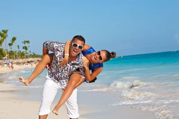 Paar hat Strandspaß huckepack — Stockfoto