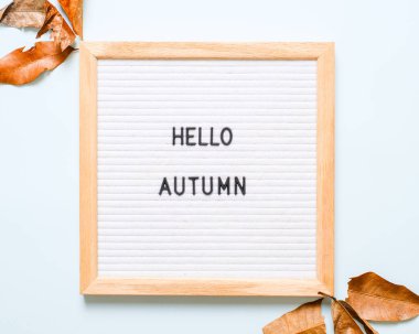 Yazıt Merhaba Ekim beyaz harf tahtasında, açık mavi arka planda kuru yapraklar. Sonbahar konsepti