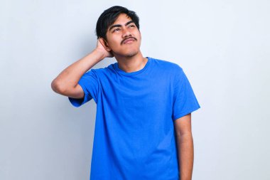 Bıyıklı, sıradan tişörtlü, beyaz arka planda duran yakışıklı genç adam soru sorup kafasını karıştırıyor. Şüpheyle kararsız, kafa kafaya düşünerek. Düşünceli kavram.