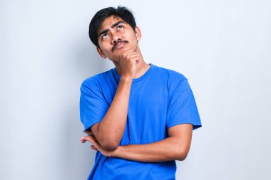 Beyaz arka plan üzerinde duran sıradan bir gömlek giyen genç yakışıklı bir soru hakkında endişeli ve gergin bir şekilde düşünüyor.