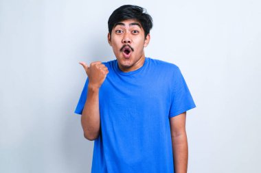 Yakışıklı Asyalı genç adam parmaklarını kenarı işaret ederek şaşkınlık ve şaşkınlık içinde beyaz arka planda korku ve şaşkınlık içinde.