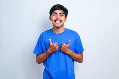 Beyaz arka plan üzerine sıradan gömlek giyen genç yakışıklı adam, olumlu bir jest yapıyor, gülümsüyor ve başarı için seviniyor. Kazanan jest.