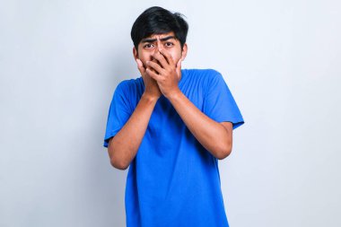 İzole edilmiş beyaz arka plan üzerine gündelik tişört giyen genç yakışıklı adam yanlışlıkla ağızlarını kapatarak şok etti. Gizli konsept.