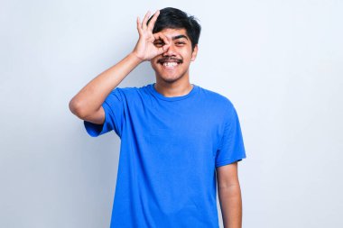 Bıyıklı yakışıklı genç adam beyaz arka plan üzerine günlük tişört giyip gülümsüyor ve el ve parmaklarıyla tamam işareti yapıyor. başarılı ifade.