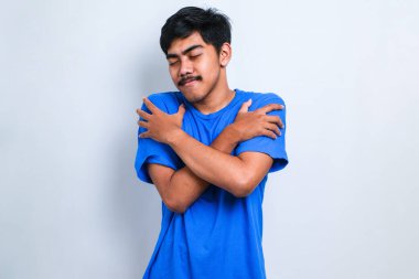 Soyutlanmış beyaz arka planda genç yakışıklı bir adam kendine sarılıyor mutlu ve pozitif, kendinden emin gülümsüyor. Sevgi ve özgüven.