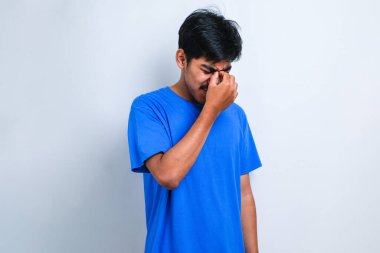 Genç yakışıklı Asyalı adam, günlük gömleğini giyiyor. İzole edilmiş beyaz arka plan üzerinde duruyor. Başı ağrıyor çünkü stres altında. Migren ağrısı..