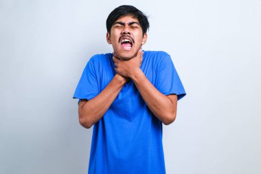 Genç yakışıklı Asyalı adam izole edilmiş beyaz arka plan üzerine günlük tişört giyip bağırıyor ve boğuluyor çünkü acı verici bir boğulma. Sağlık problemi. Boğulma ve intihar konsepti.