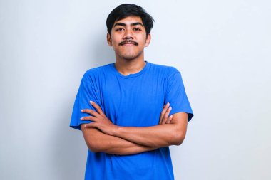 Beyaz arka plan üzerine gündelik tişört giyen genç yakışıklı kollarını kavuşturup kameraya bakarak gülümsüyor. pozitif kişi.