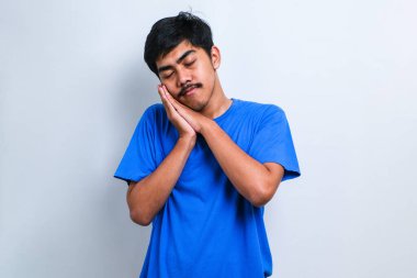 Asyalı yakışıklı bir adam tişört giyer, uyur, yorgun düşler görür, el ele poz verir, beyaz arka planda gözleri kapalı gülümserdi.