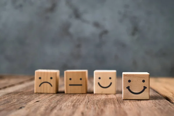 Customer service evaluation and satisfaction survey service rating concepts. Close up customer hand choose the happy face smile face icon on wooden cube on table.