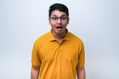 Şaşırmış Asyalı genç adam, ağzı açık, gözleri şişmiş, kameraya bakıyor, izole beyaz arka plan.
