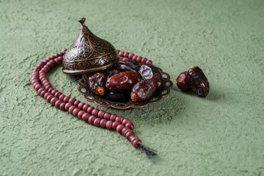 Eski yeşil ahşap masa üzerinde hurma ve tasbih olan klasik bir tabak. Ramazan arka planı. Düz yatıyordu.
