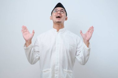 Asyalı Müslüman bir adam ellerini uzatarak onlara yukarıdan ulaşan ve beyaz arka planda izole edilmiş bir şeyden korunuyor.