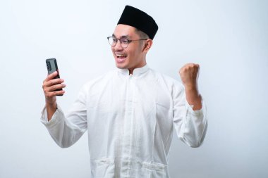 Akıllı telefon tutan Asyalı Müslüman adam, elinde cep telefonu tutarak kazanıyor Happy, beyaz arka planda izole edilmiş özel bir hediye alıyor.