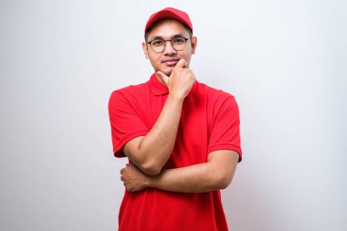 Yakışıklı Asyalı teslimatçı, izole edilmiş beyaz arka planda duruyor. Kameraya kendinden emin bir şekilde bakıyor. Kollarını kavuşturup, çenesini kaldırarak gülümsüyor. Olumlu düşünüyorum..