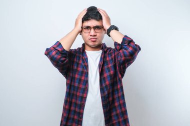 Genç yakışıklı Asyalı adam, günlük gömleğini giyiyor. İzole edilmiş beyaz arka plan üzerinde duruyor. Başı ağrıyor çünkü stres altında. Migren ağrısı..