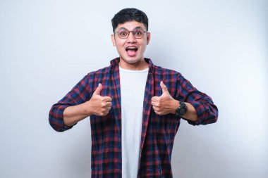 Beyaz arka plan üzerine sıradan gömlek giyen genç yakışıklı adam, olumlu bir jest yapıyor, gülümsüyor ve başarı için seviniyor. Kazanan jest.