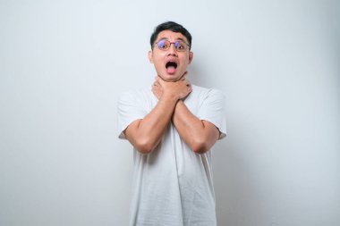 Yakışıklı Asyalı genç adam izole edilmiş beyaz arka plan üzerine gündelik tişört giyip bağırıyor ve boğuluyor çünkü acı verici bir boğulma. Sağlık problemi. Boğulma ve intihar konsepti.