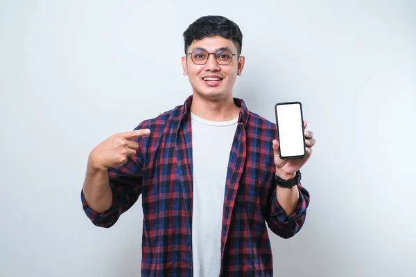 Asian young man wearing casual shirt and glasses smile looking to camera showing blank smartphone screen recommending application, isolated on white background
