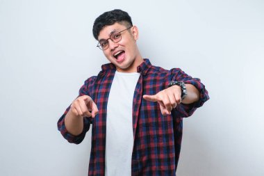 Beyaz arka plan üzerinde duran Asyalı genç ve yakışıklı bir adam parmaklarıyla seni ve kamerayı işaret ediyor, neşeli ve pozitif gülümsüyor.