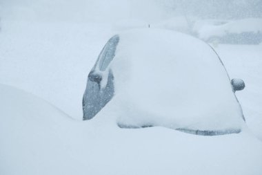 Park halindeki küçük bir araba, kış fırtınası sırasında bir banliyö sokağında kısmen kara gömülür..