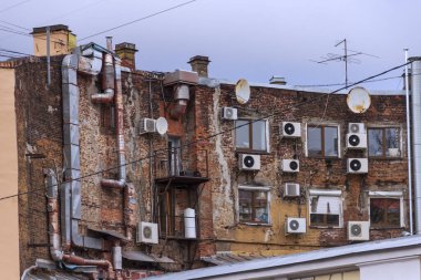 Asılan klimaları olan tuğladan bir binanın arka duvarı. Boruları, kabloları, havalandırması ve antenleri olan eski bir evin avlusu..