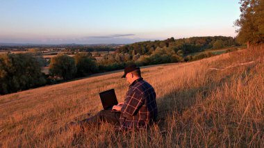 Man using laptop sitting on a hill in the countryside