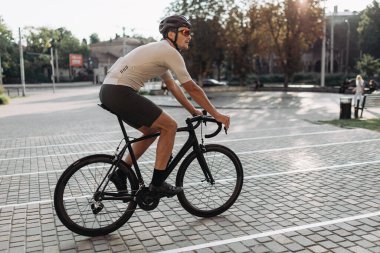 Spor elbiseli, kasklı ve gözlüklü beyaz sporcu şehir caddesinde bisiklet sürüyor. Profesyonel bisikletçi, sabah sporunu dışarıda yapıyor. Sağlıklı yaşam tarzları konsepti.