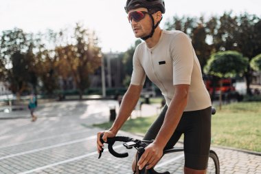 Kasklı ve aynalı gözlüklü aktif bir beyaz adam şehir caddesinde bisiklet sürüyor. Boş zamanlarında dışarıda egzersiz yapan güçlü bir bisikletçi..