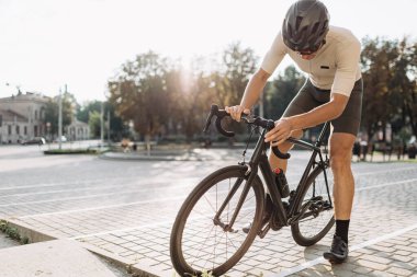 Beyaz erkek sporcu, temiz havada bisiklet sürdükten sonra dinleniyor. Açık havada siyah bisiklette oturan güçlü bir adam. Arkaplanda güneş ışığı.