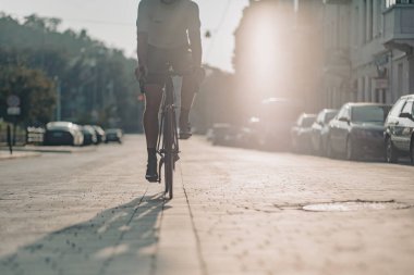 Şehir caddesinde bisiklet süren spor kıyafetli aktif kaslı adamı kapatın. Arka planda güneş ışığı var. Profesyonel bisikletçinin düzenli eğitimi.