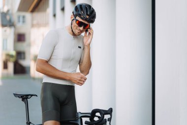 Kafkasyalı bir adam kulağının yanında multimedya navigatörü tutuyor ve gülümsüyor. Spor kıyafetleri içinde yakışıklı bir adam temiz havada bisikletle sabah mesafesini kontrol ediyor..