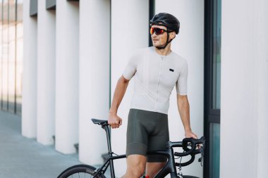 Beyaz erkek sporcu, sabah bisikletçisi olarak dışarı çıkıyor. Bisiklette oturan ve yan yan bakan olumlu genç adam. Favori spor hobisi.