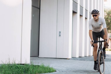 Kasklı ve gözlüklü beyaz bir adam şehir merkezinde bisiklet sürüyor, kopyalama alanı. İnsan kavramı, eğitim ve favori hobi.