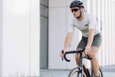 Spor kıyafetleri, kask ve gözlük takan erkek sporcu sabah vaktini temiz havada bisiklet sürmek için harcıyor. Erkek kişi üzerinde etkin eğitim için kentsel alan.
