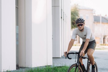 Büyük şehrin sokaklarında boş zamanlarında spor elbiseli, kasklı ve gözlüklü bisiklet süren beyaz bir bisikletçi. Dayanıklılık, güç ve motivasyon kavramı.