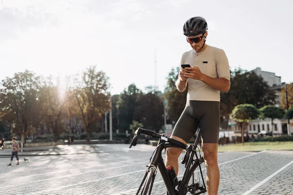 Mężczyzna Sportowiec Kasku Okulary Siedzi Czarnym Rowerze Nowoczesnym Smartfonem Rękach — Zdjęcie stockowe